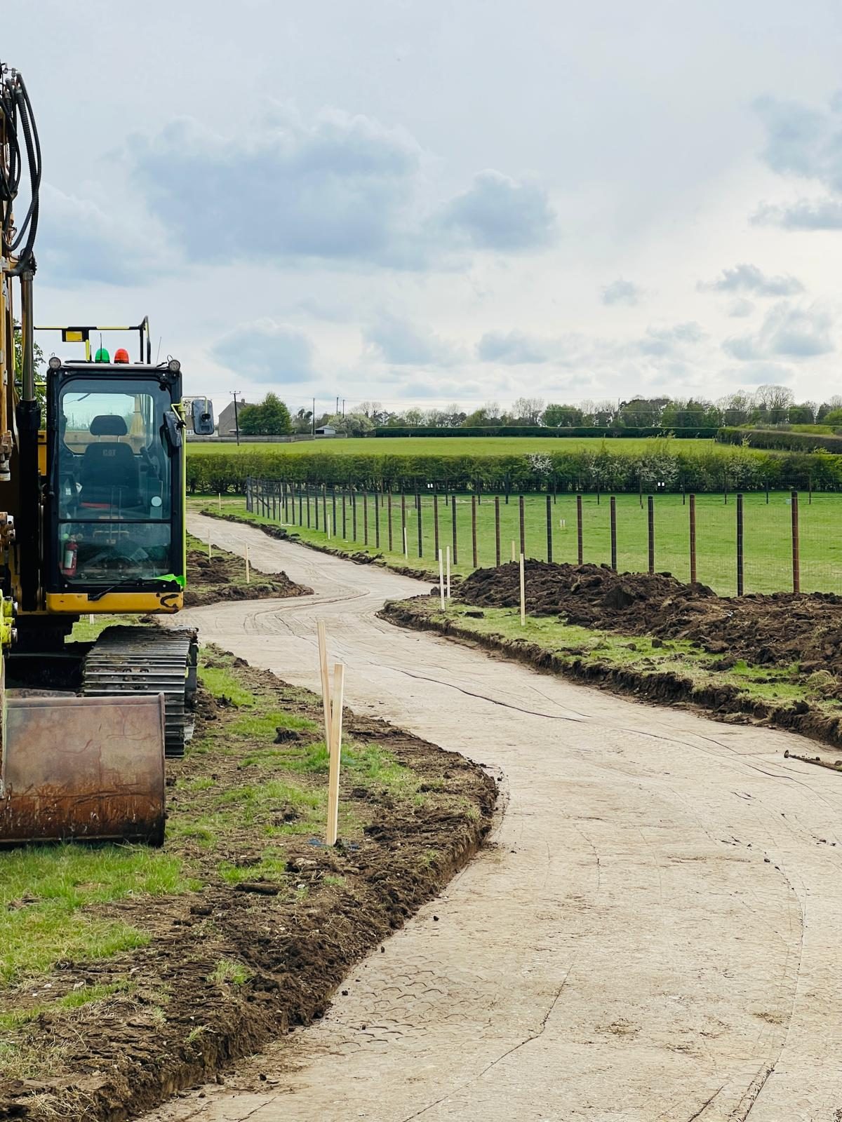 A newly formed haul road curving through fields at a 24MW solar site in Cambridgeshire, with new perimeter fencing being installed.