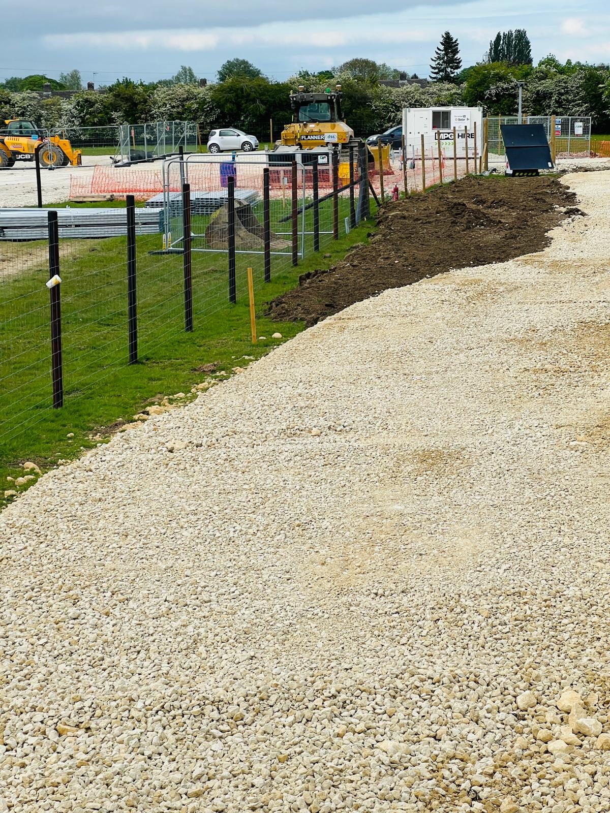 A finished crushed-stone access road curving through a 24MW solar site in Cambridgeshire.