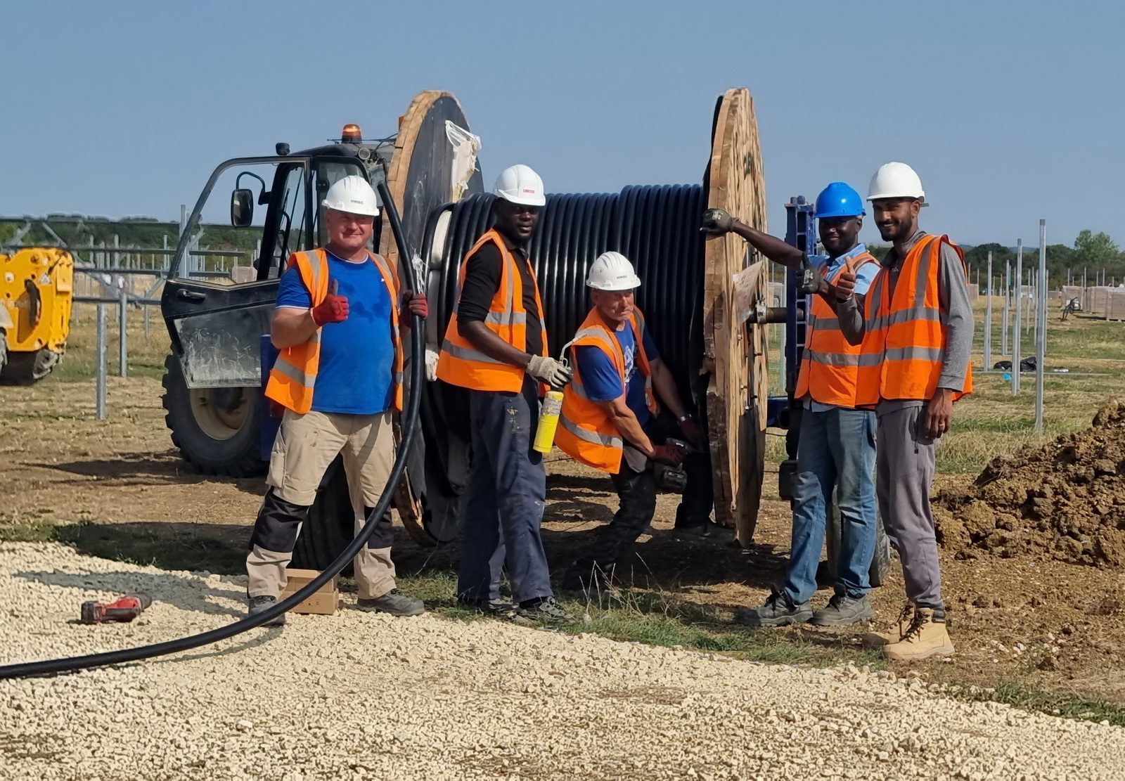 Five HWBC operatives in branded helmets working with a cable drum at a 29MW solar site in Oxfordshire.