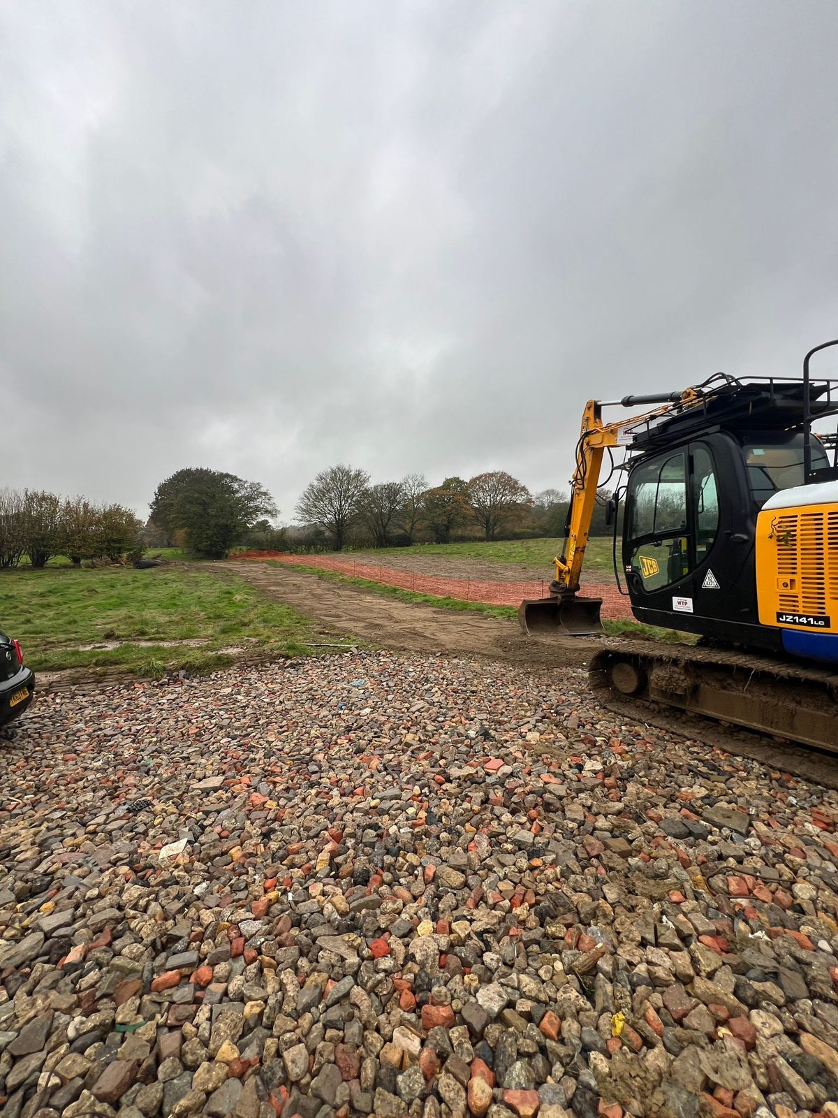 A JCB beside a newly stoned access track running through fields at a solar site.