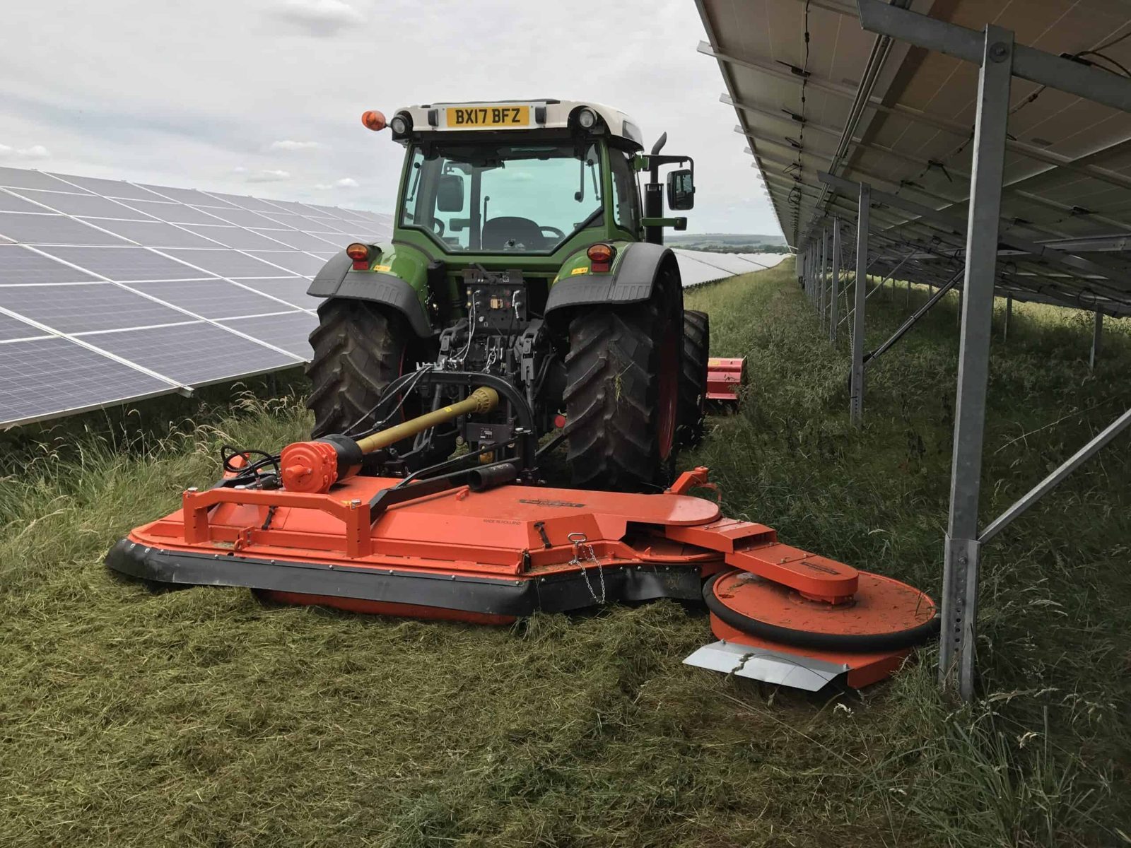 A tractor mowing vegetation between solar panel rows during site maintenance.