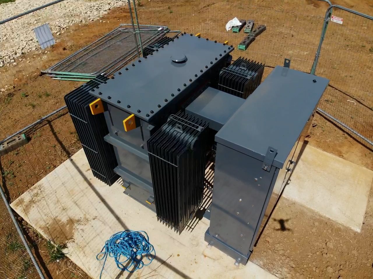 Aerial view of a transformer set on its base within a fenced compound.